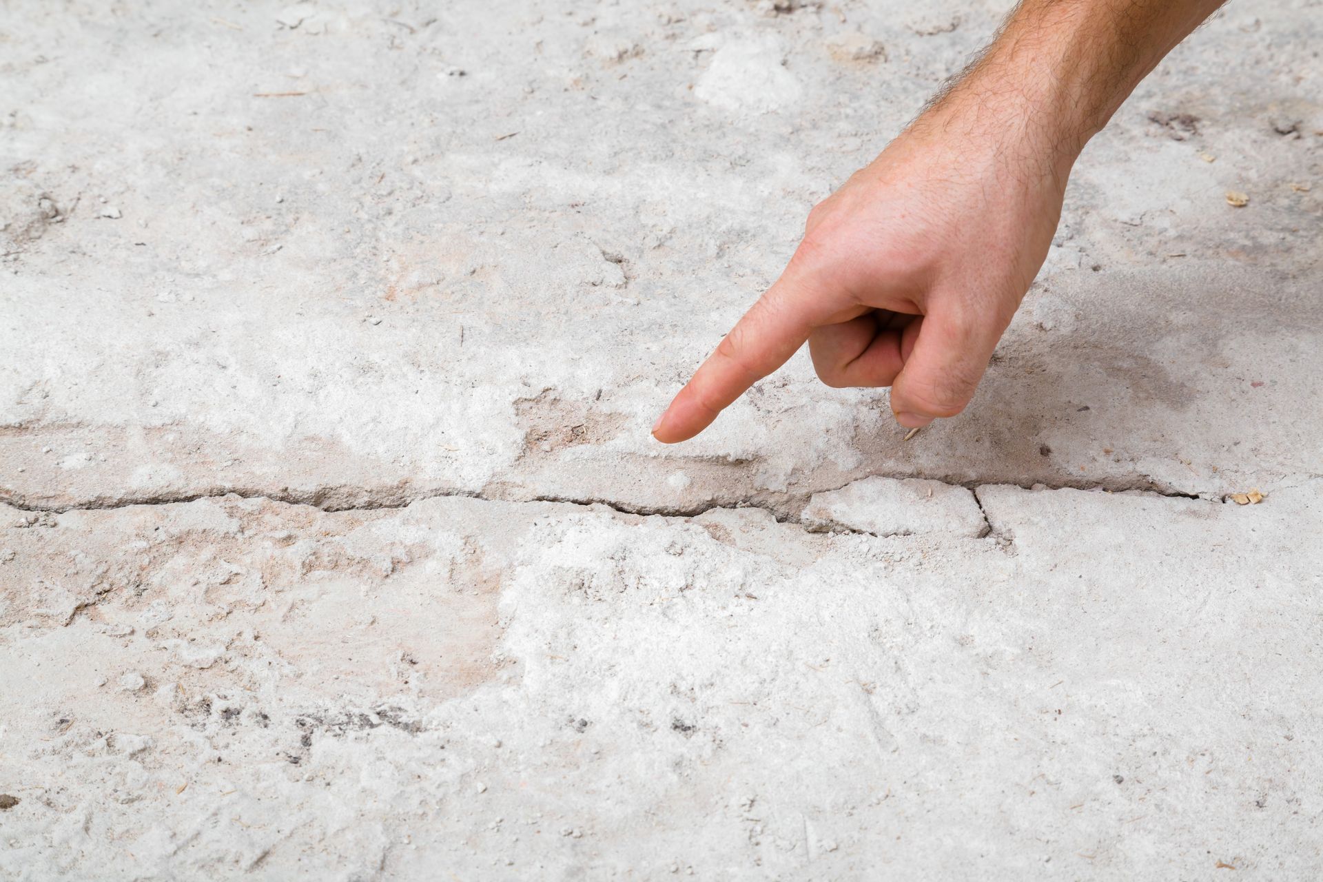 A hand pointing to a crack in a white concrete surface