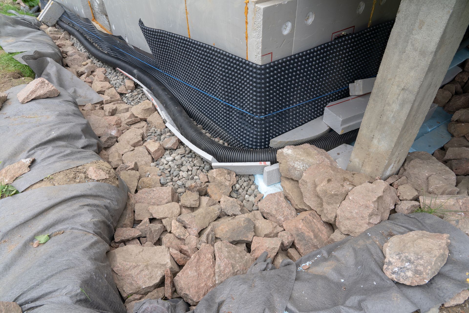 Black drainage wrap around building foundation with rubble and rocks in a construction area