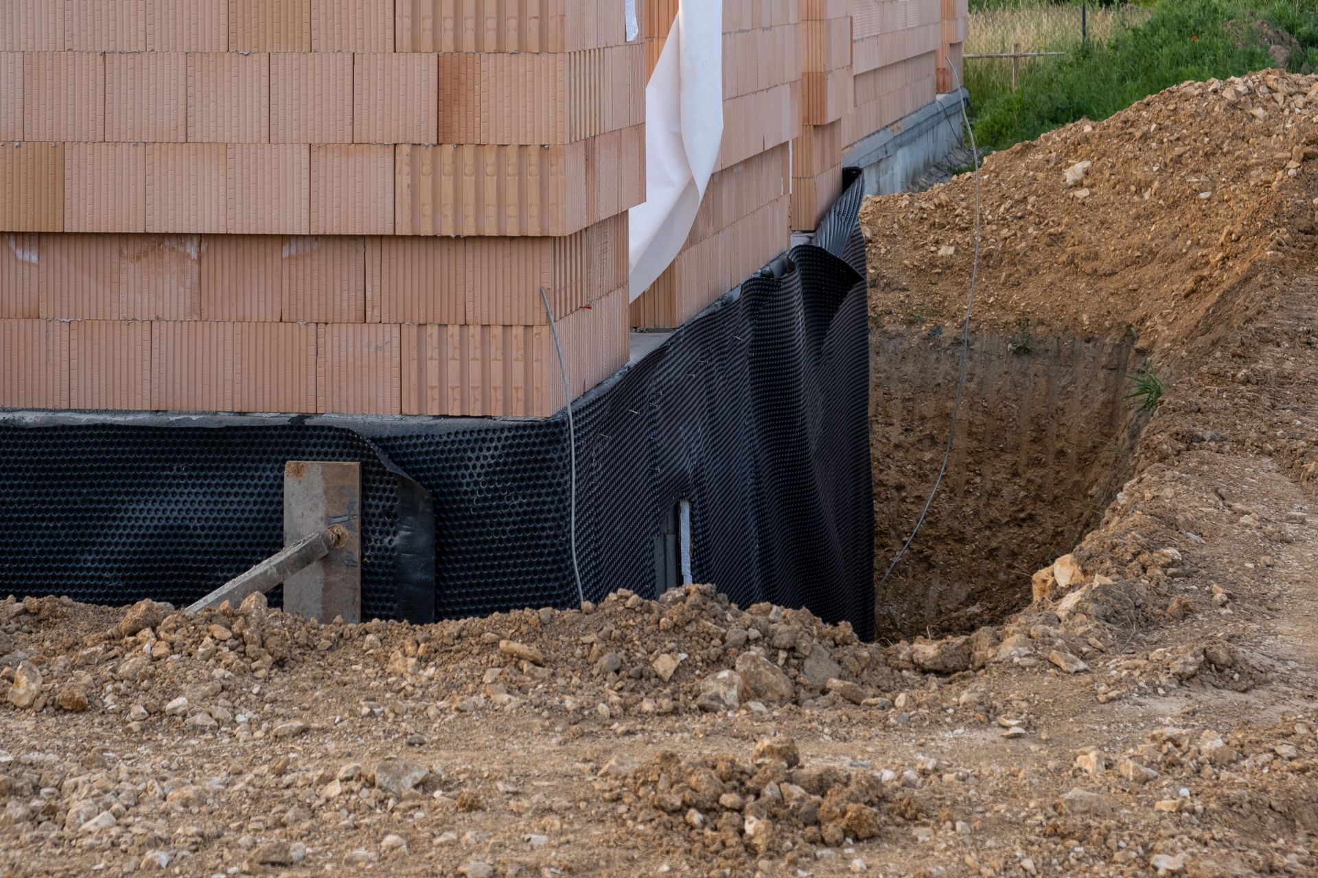Construction site with foundation waterproofing beside a brick wall and excavated dirt.