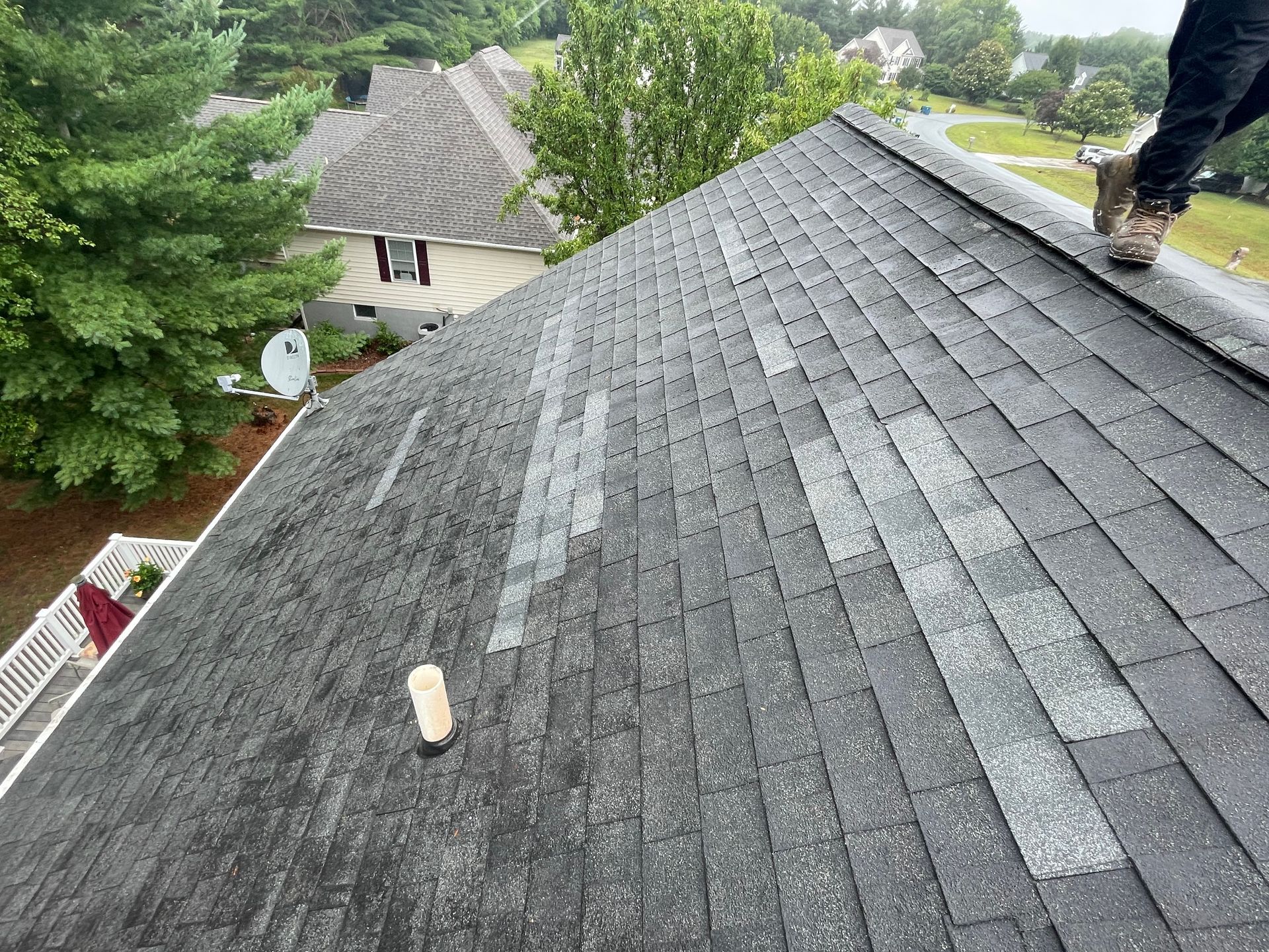 Roof with missing shingles; person stands on the edge. Gray shingles with patches of lighter areas; residential setting.