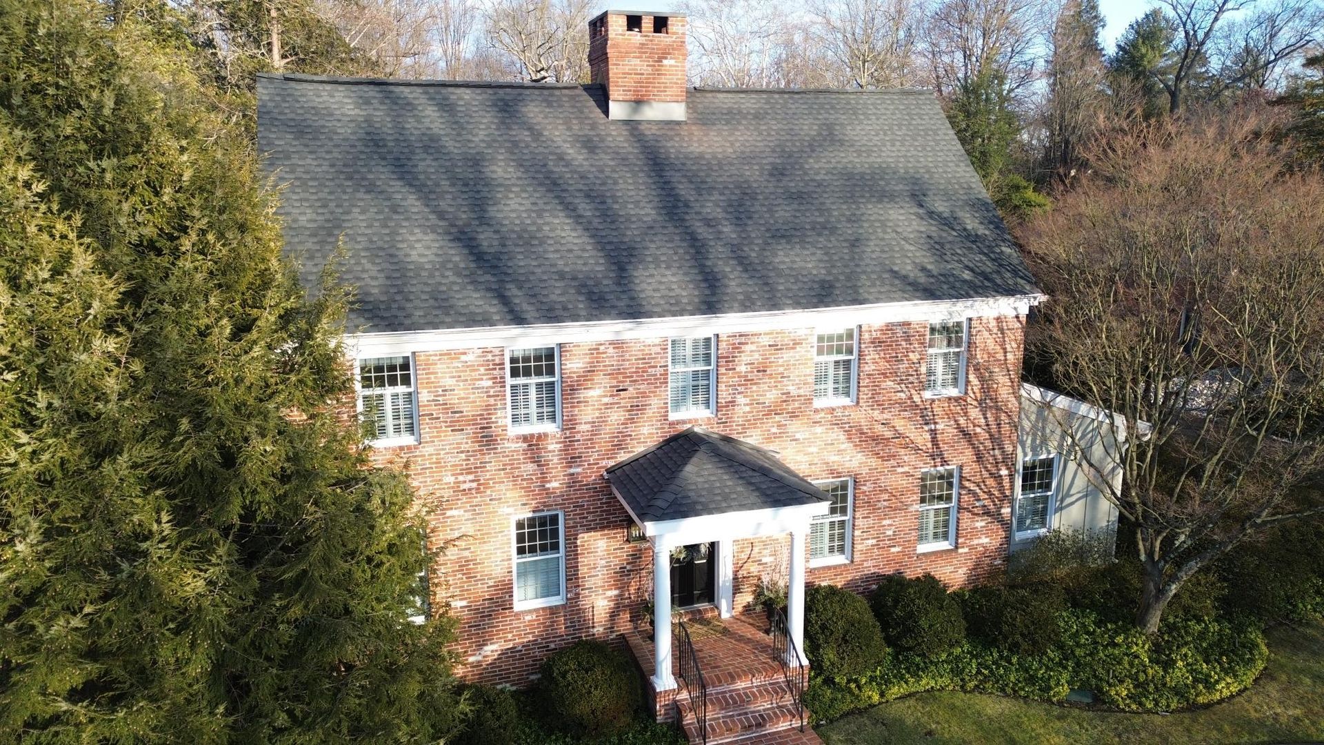 Two-story brick house with dark roof and white-trimmed windows; front porch under a black roof.