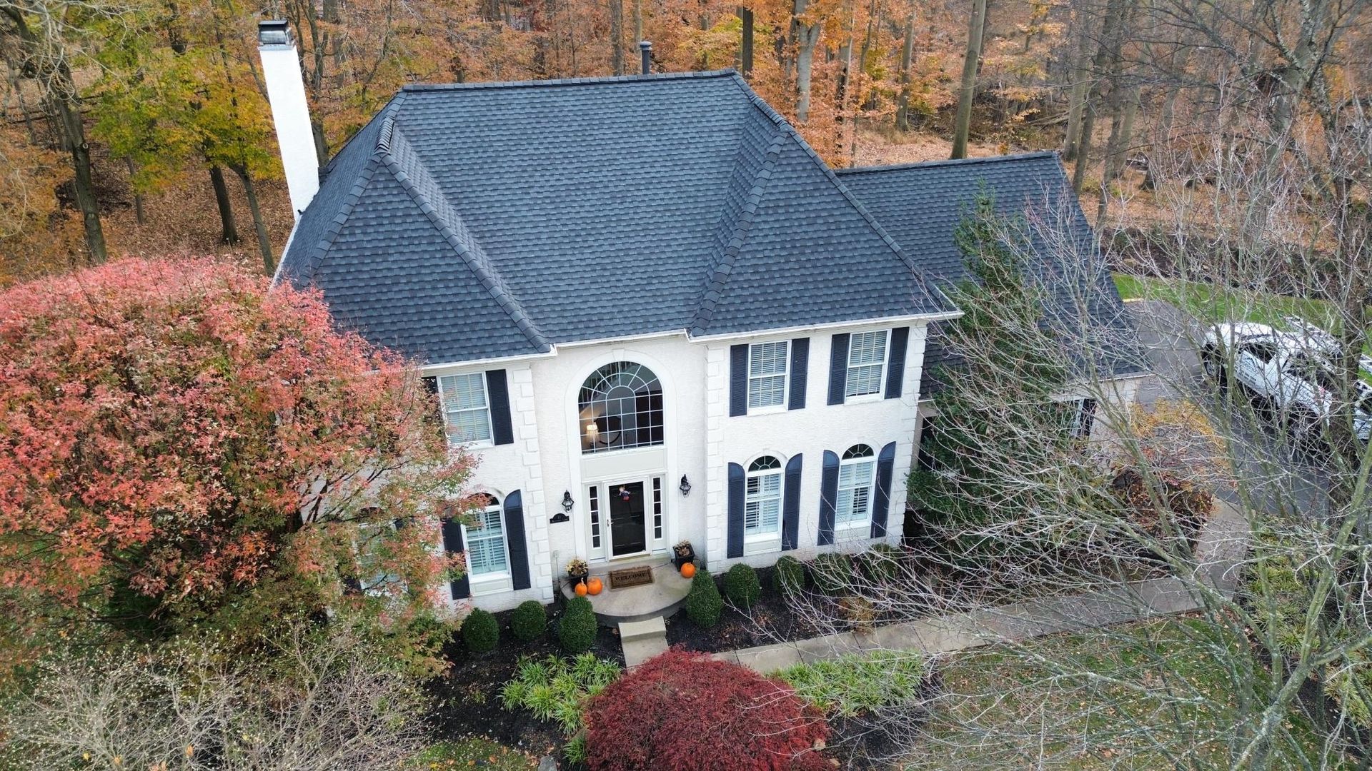Two-story white house with black shutters, dark blue roof, and fall foliage.