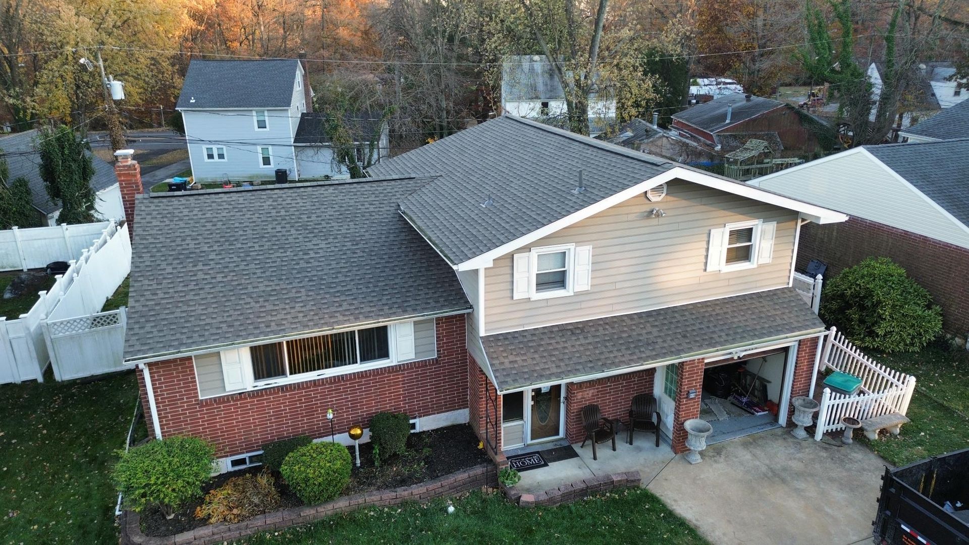 Aerial view of a two-story house with a gray roof and brick and tan siding, surrounded by trees and other houses.