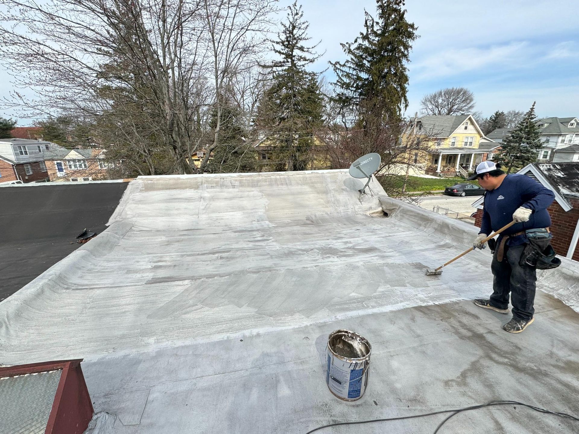 A man is painting a roof with a broom.