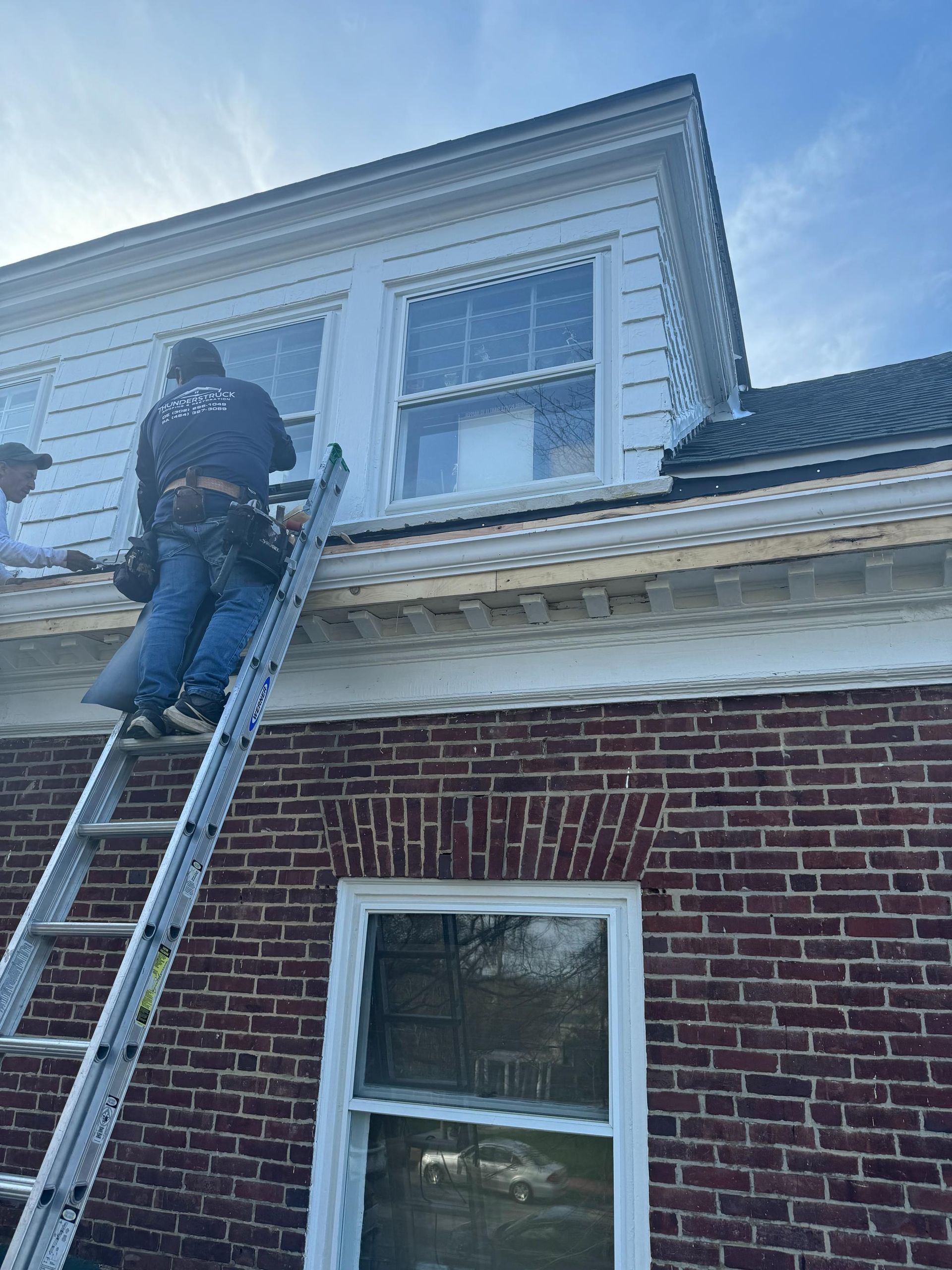 A man is standing on a ladder on the roof of a brick building.
