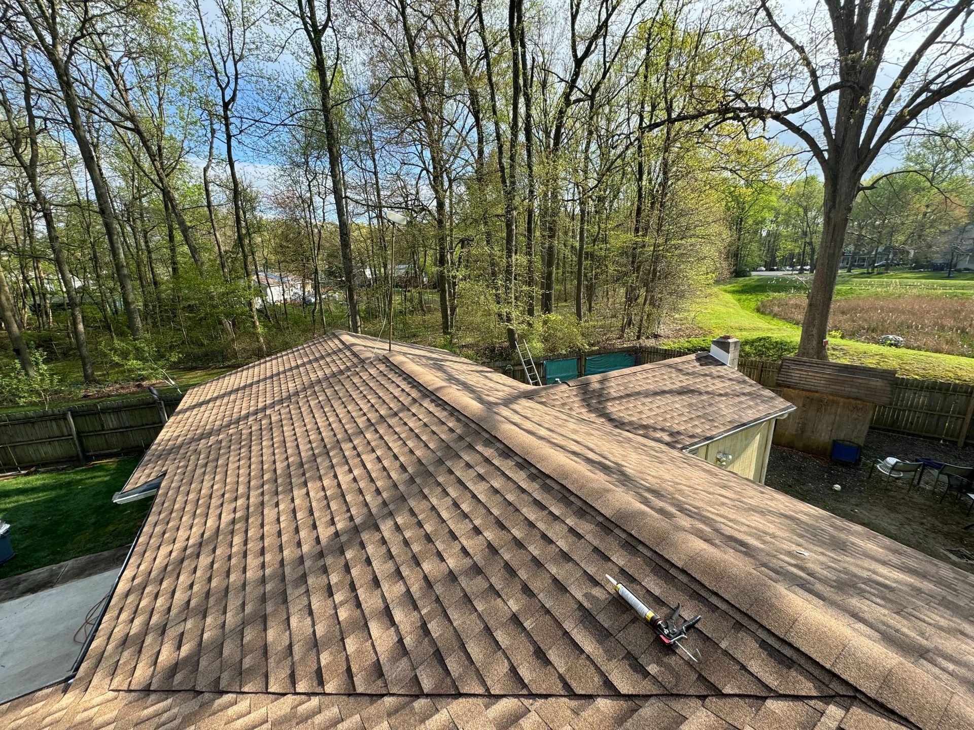 The roof of a house with trees in the background and a pool in the backyard.