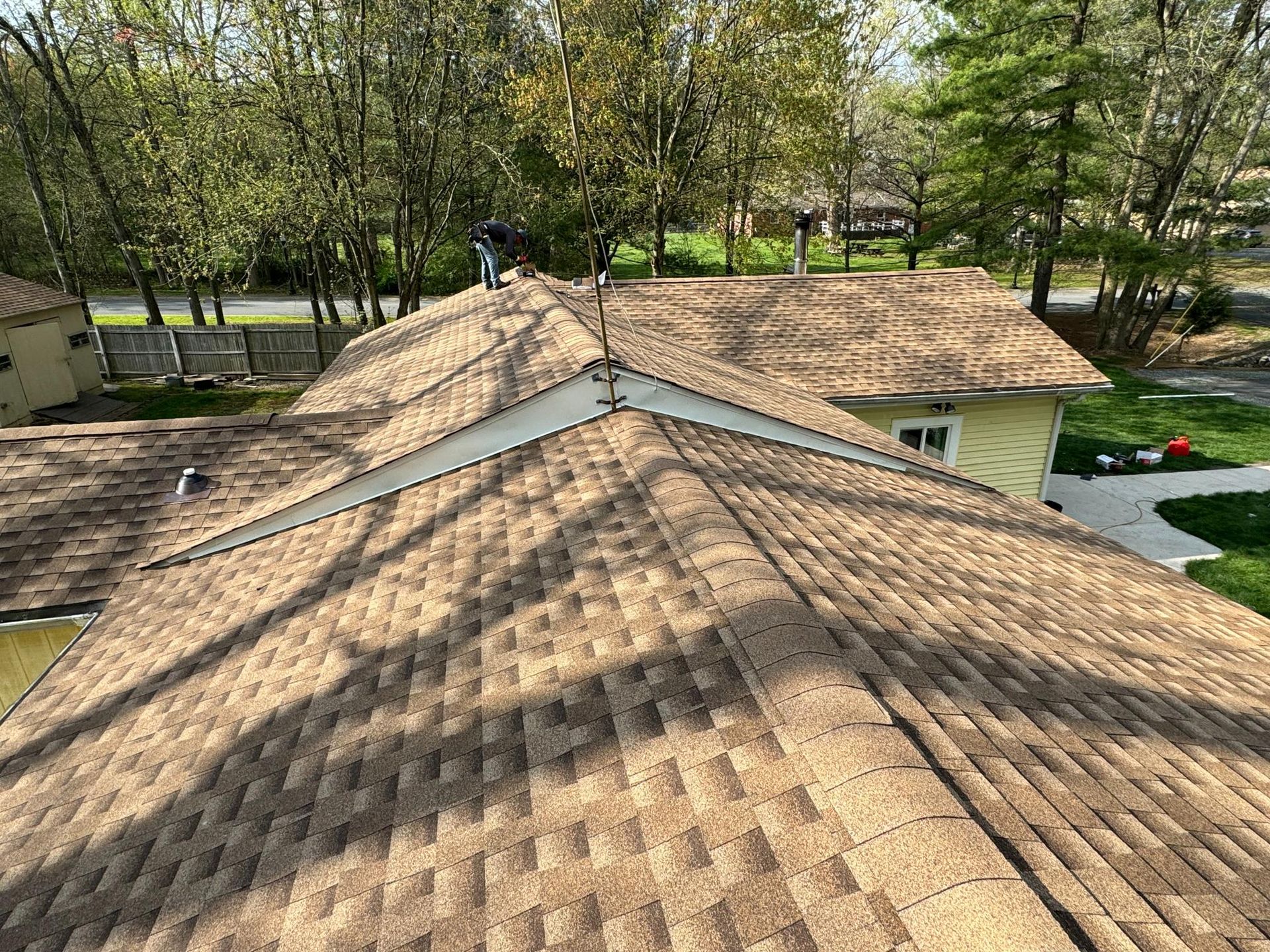 A rooftop with two workers installing shingles on a sunny day.