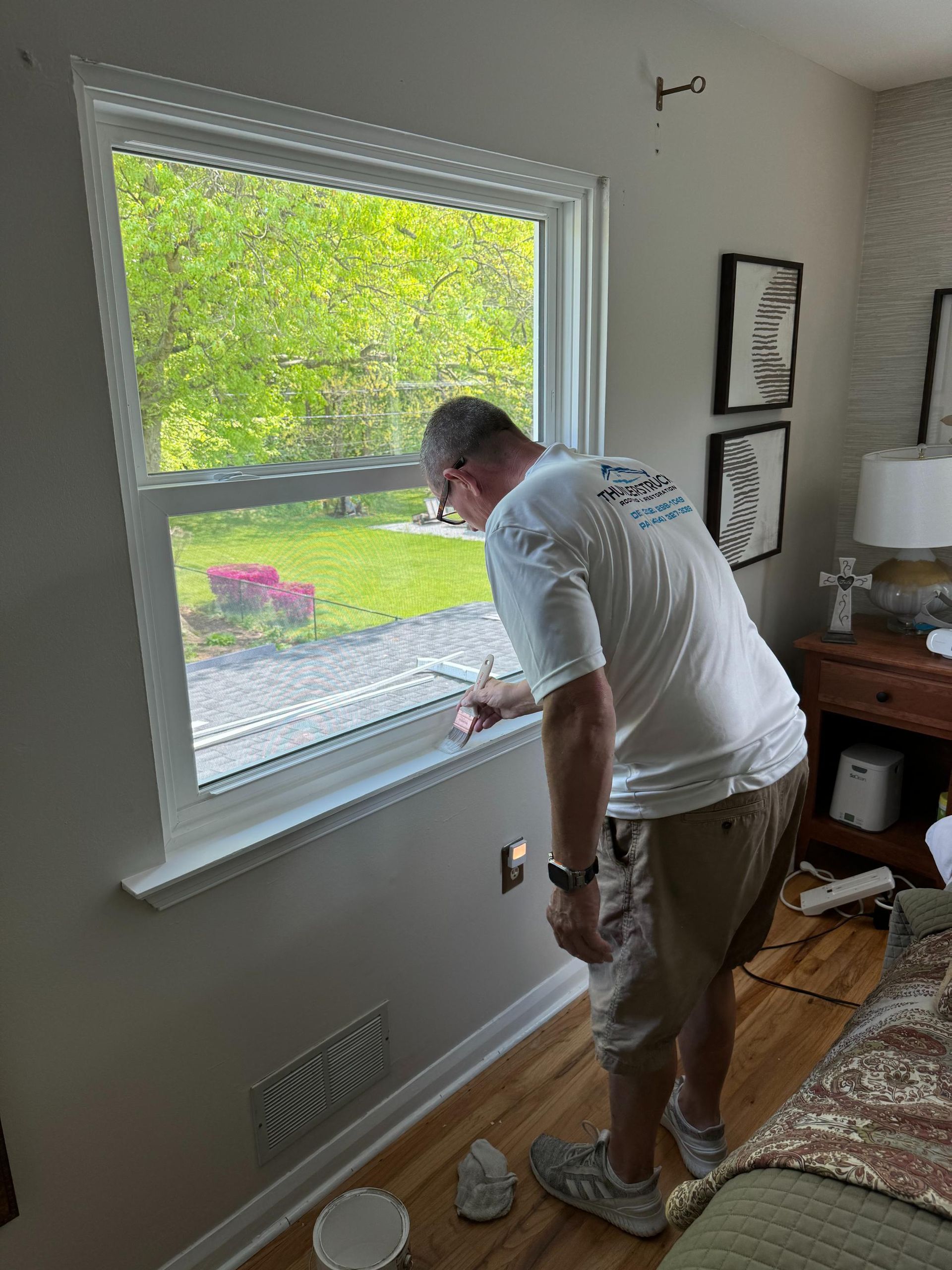 A man is painting a window in a living room.