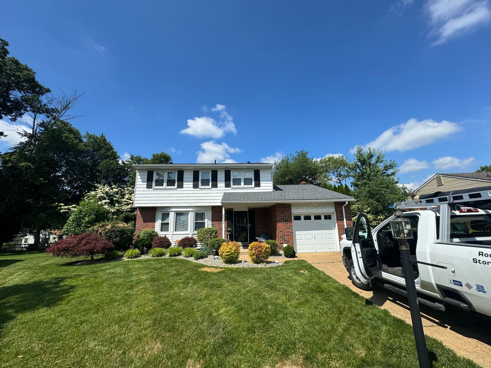A white truck is parked in front of a brick house.