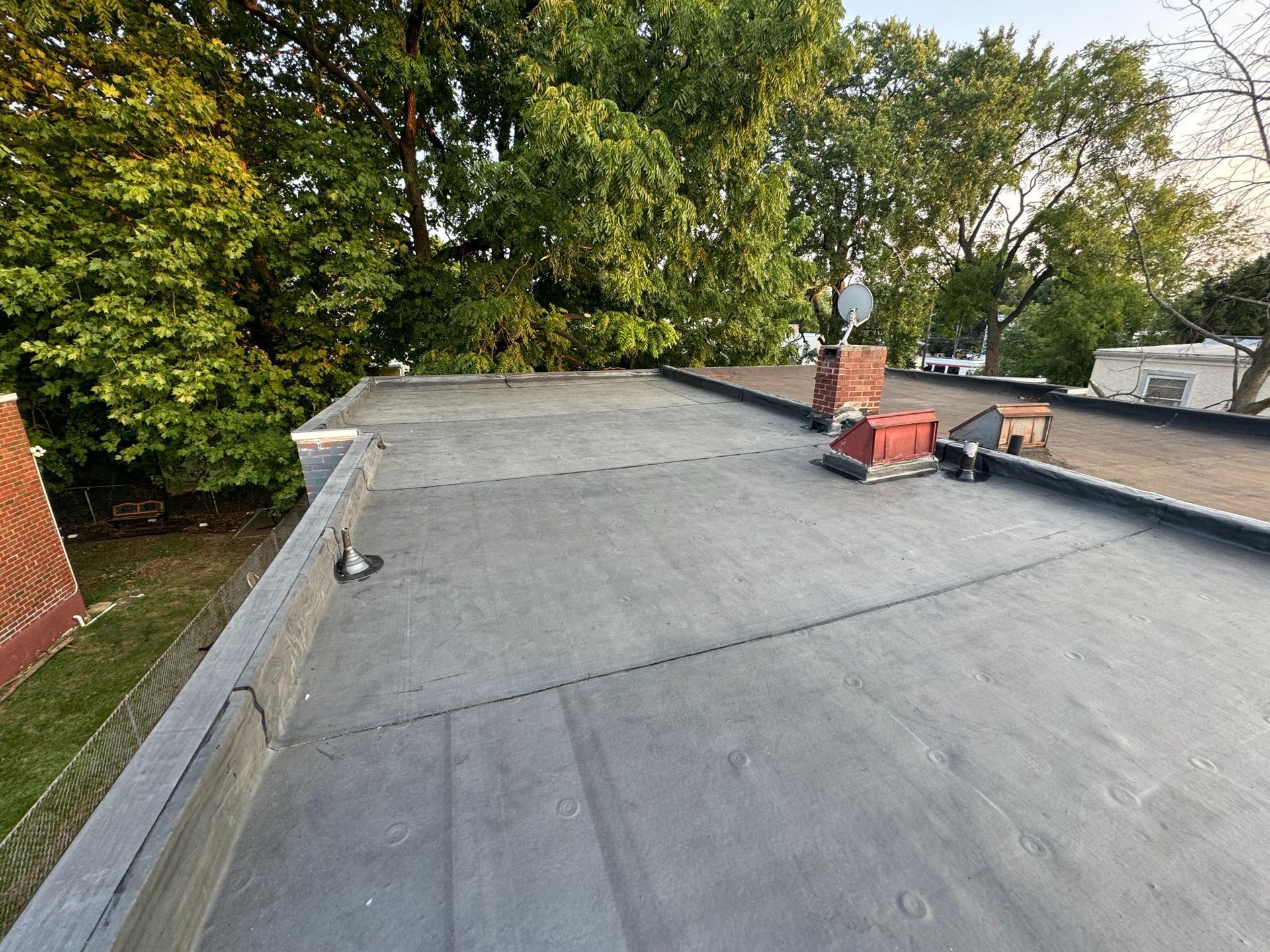 A roof with a chimney on it and trees in the background.
