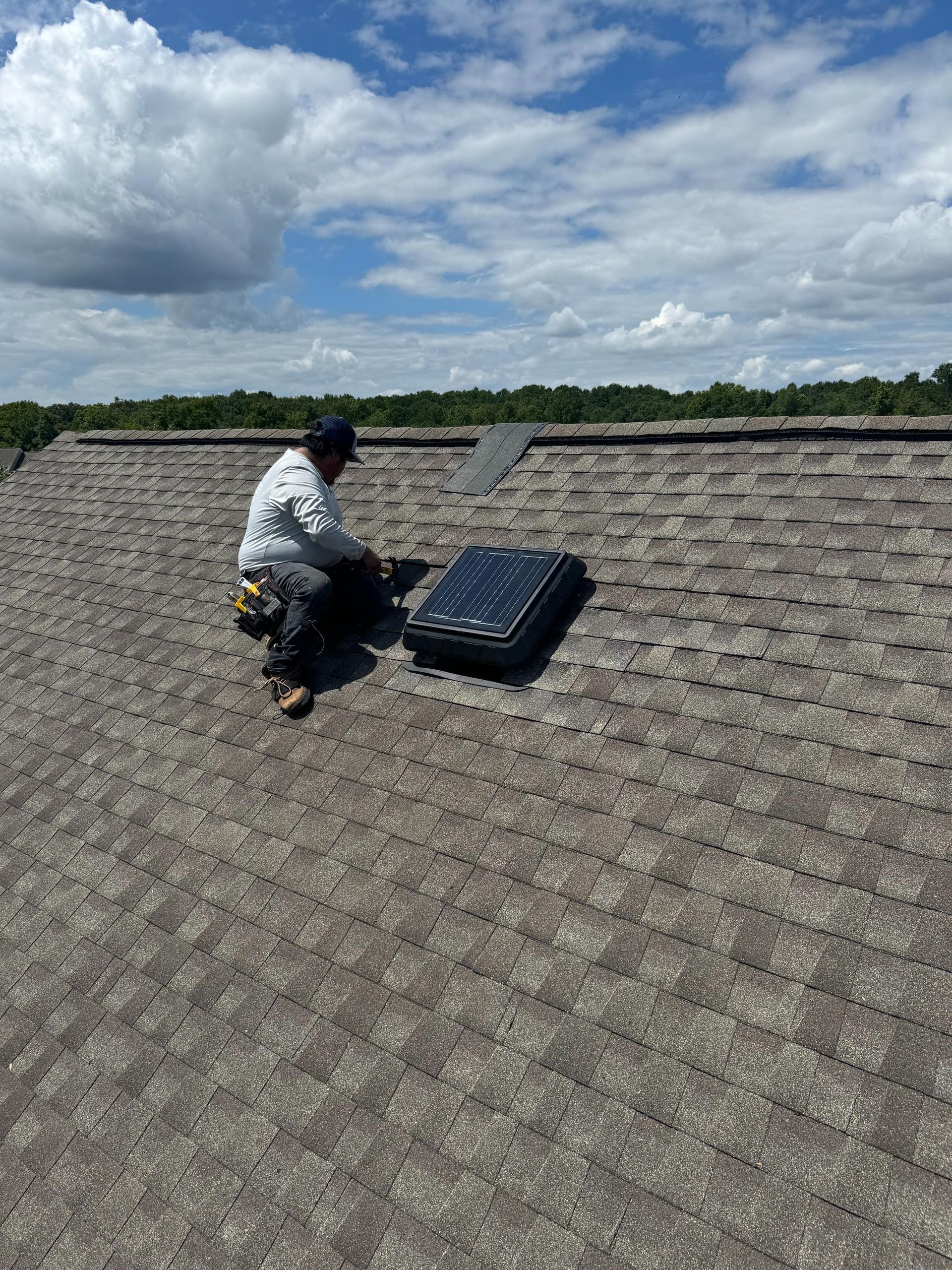 A man is kneeling on a roof working on a solar panel.
