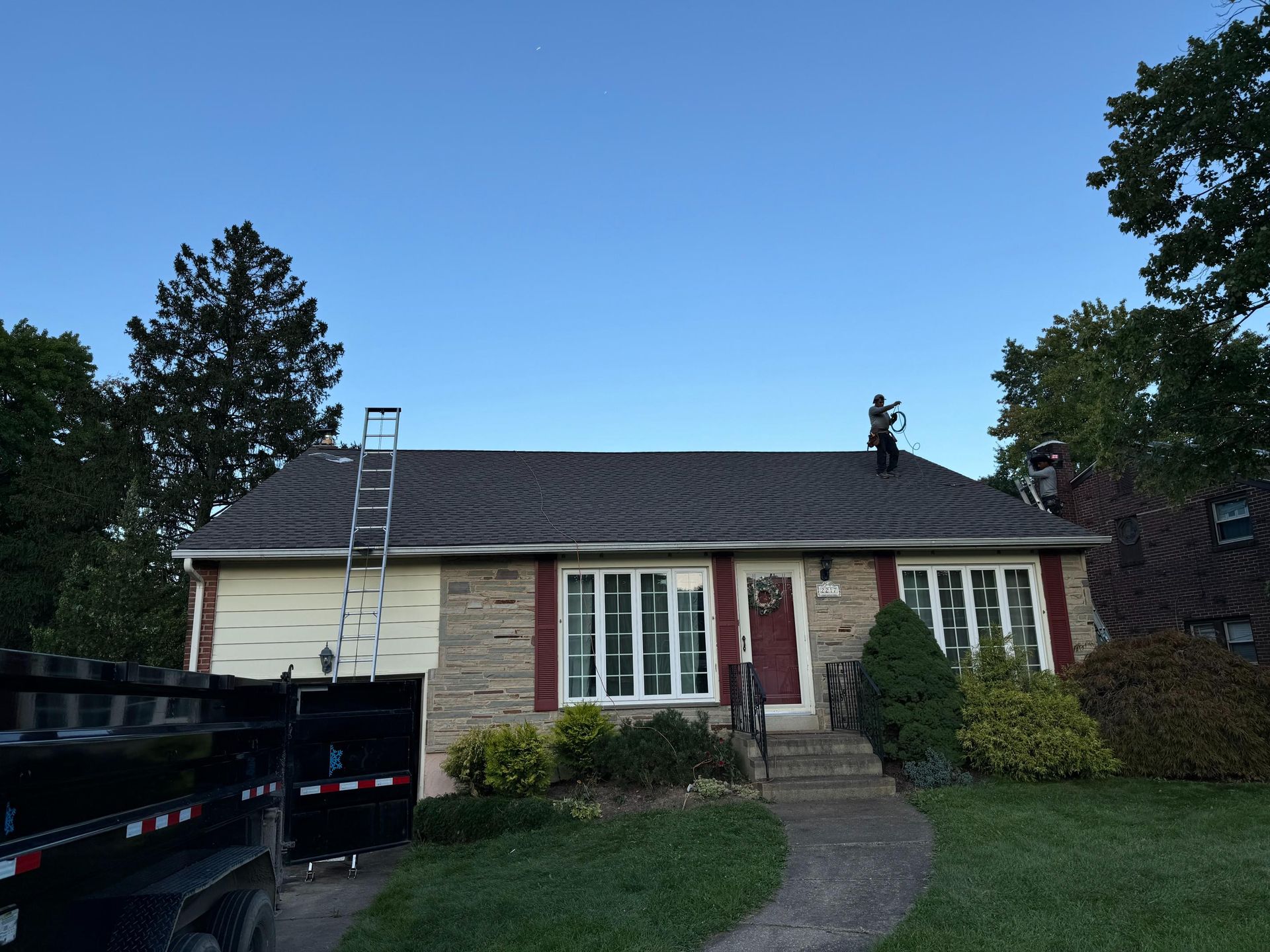 A house with a ladder on the roof and a dumpster in front of it.