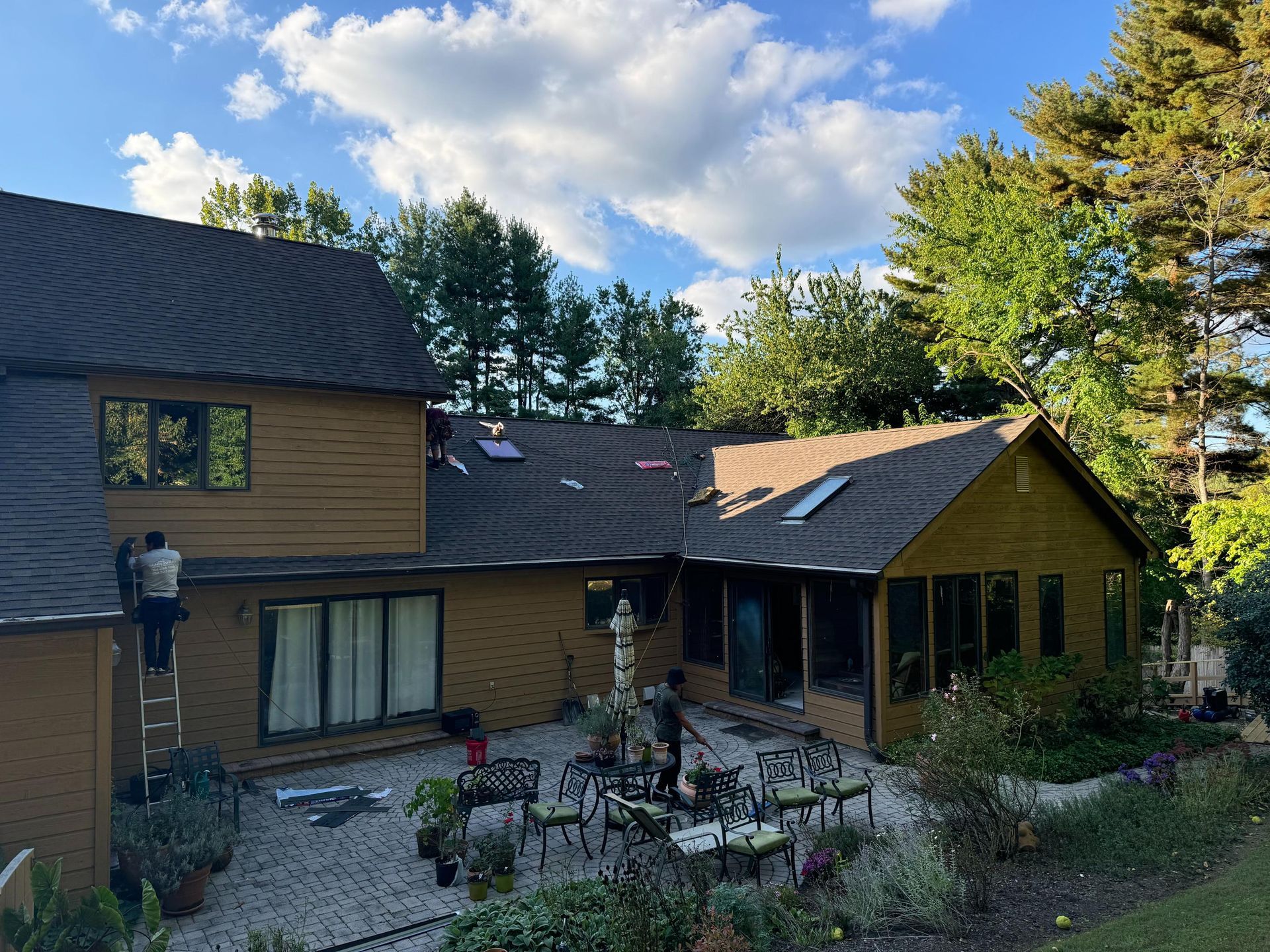 A man is standing on a ladder on the roof of a house.