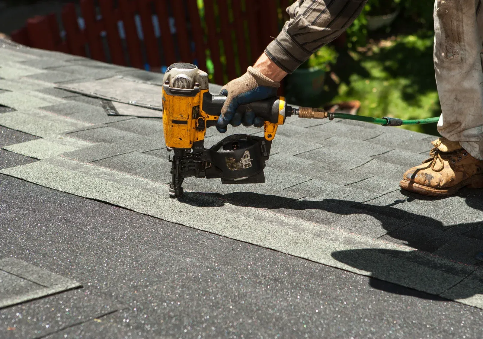 Roofer using a nail gun to install asphalt shingles on a roof.
