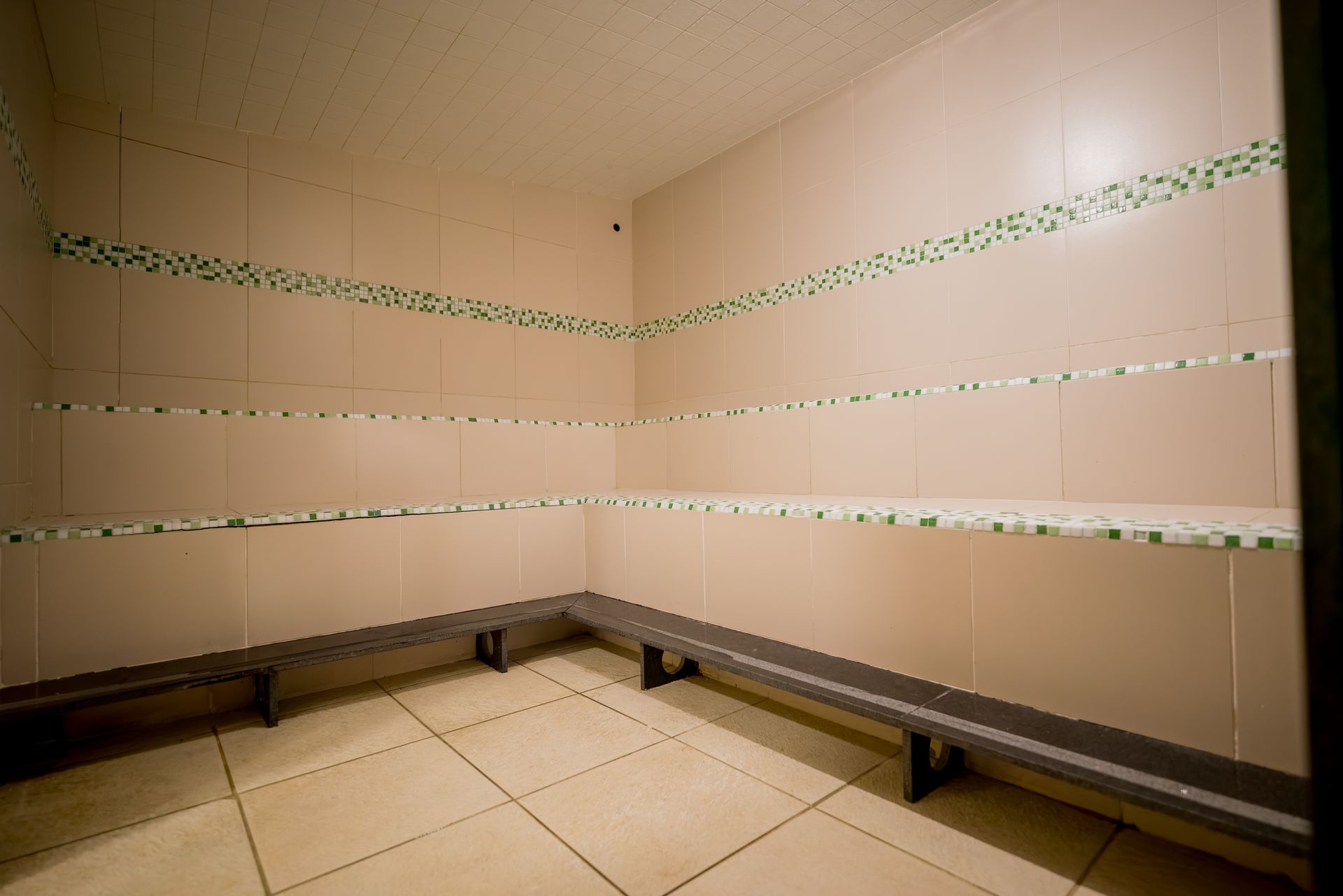Vestiário vazio com piso de azulejo, bancos e prateleiras.