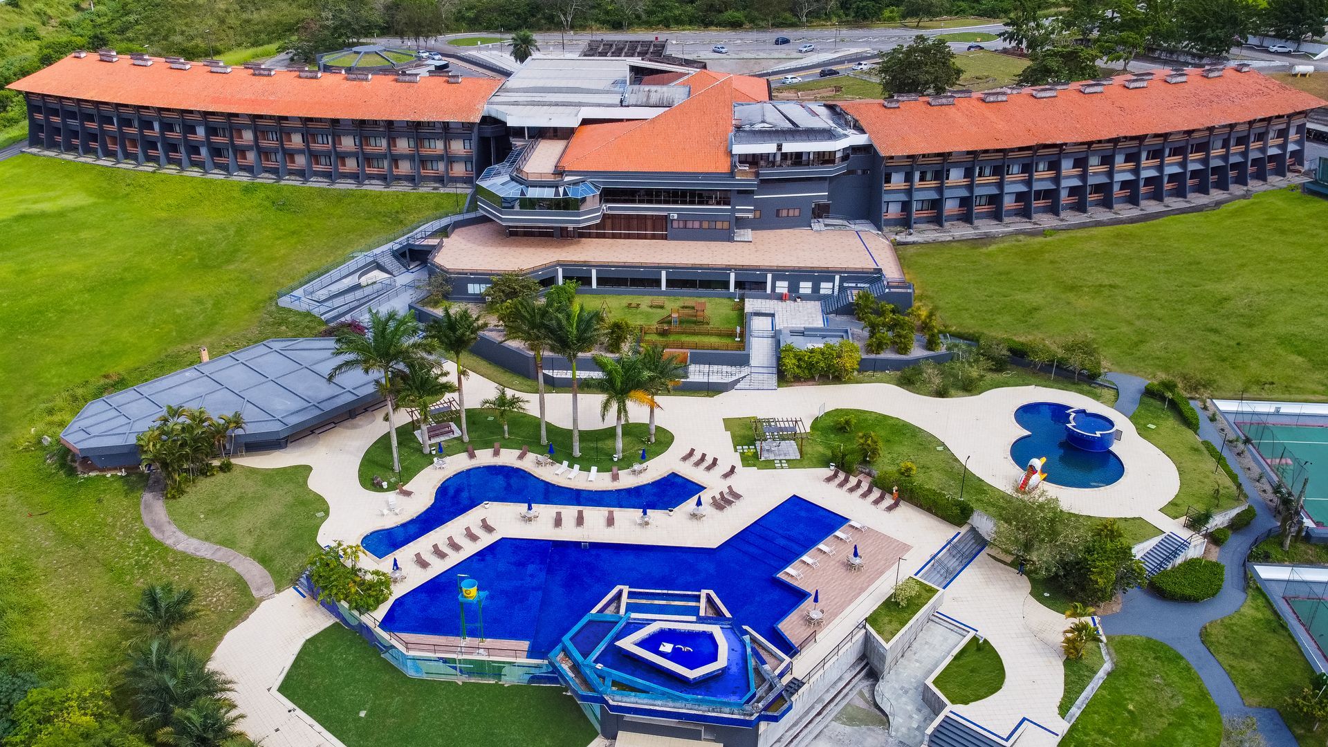 Vista aérea de um resort com piscinas, edifícios e paisagem verdejante.