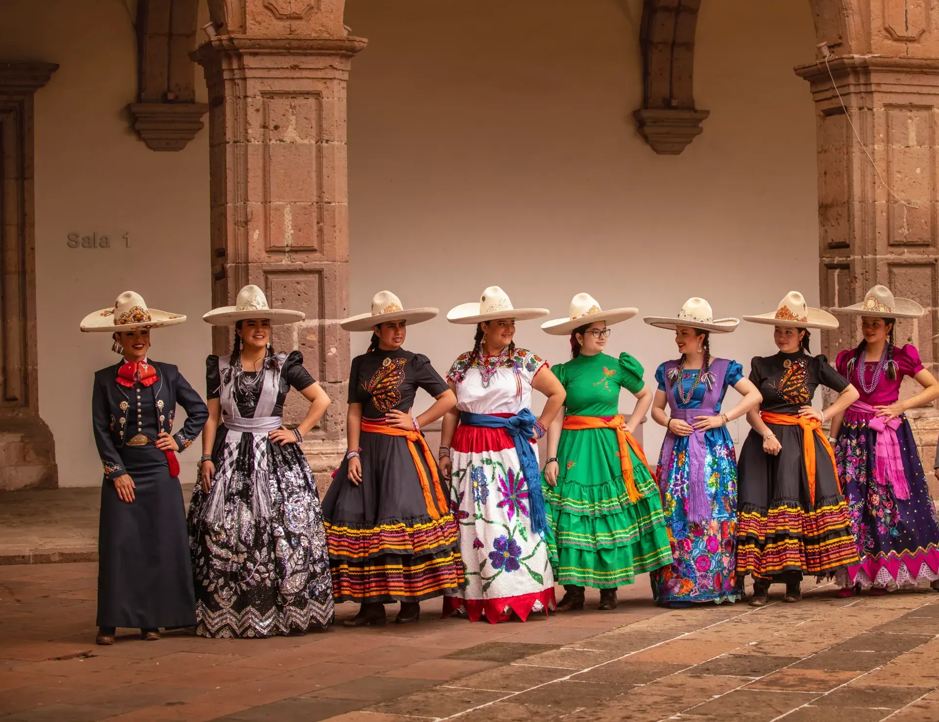 Un grupo de mujeres con vestidos y sombreros tradicionales mexicanos están de pie en una fila.