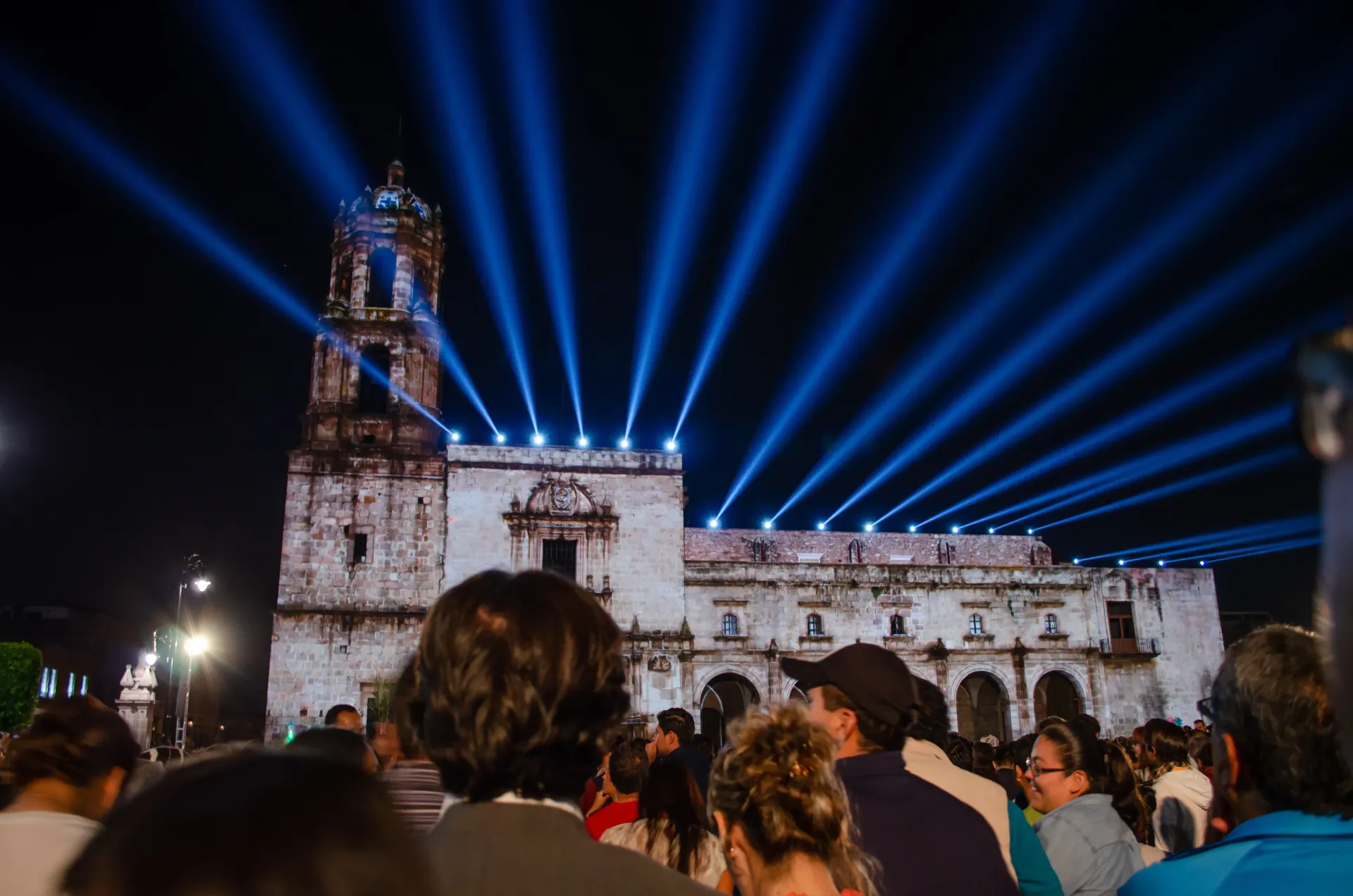A crowd of people are watching a light show in front of a building.