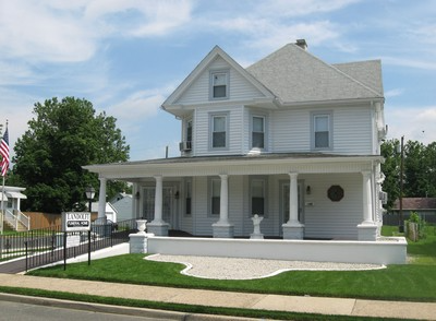 White two-story house with a wraparound porch and white columns on a sunny suburban street