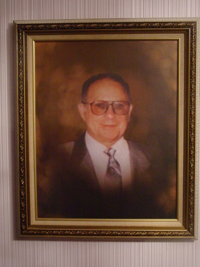Framed portrait of a smiling man in a suit and tie against a brown background