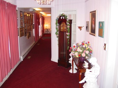 Red-carpeted hallway with framed art, a clock cabinet, and a floral arrangement on a white pedestal