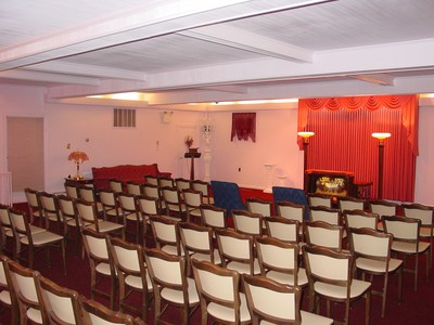 Empty banquet hall with rows of white chairs facing a red-curtained stage and fireplace