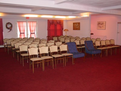 Empty conference room with rows of beige chairs, blue armchairs, and red carpet near curtained windows.