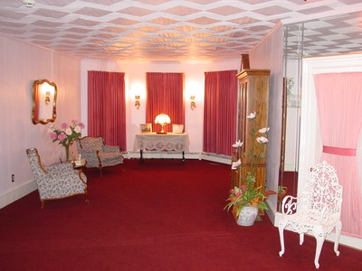 Elegant pink lounge with red carpet, floral chairs, draped curtains, and a white ornate chair