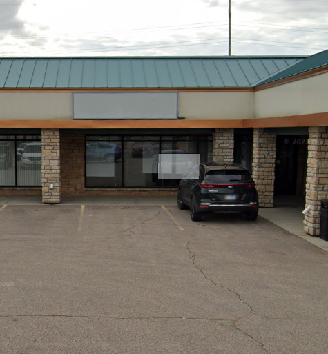 Exterior of a one-story commercial building with a black car parked in front. The building has a blank sign.