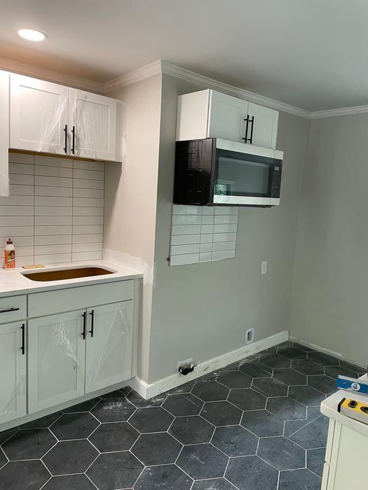 Small kitchen with white cabinets, gray hex tile floor, and a wall-mounted microwave over tile backsplash.