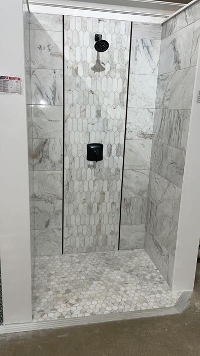 Partially tiled shower stall with marble-look walls, pebble floor, and black shower fixtures