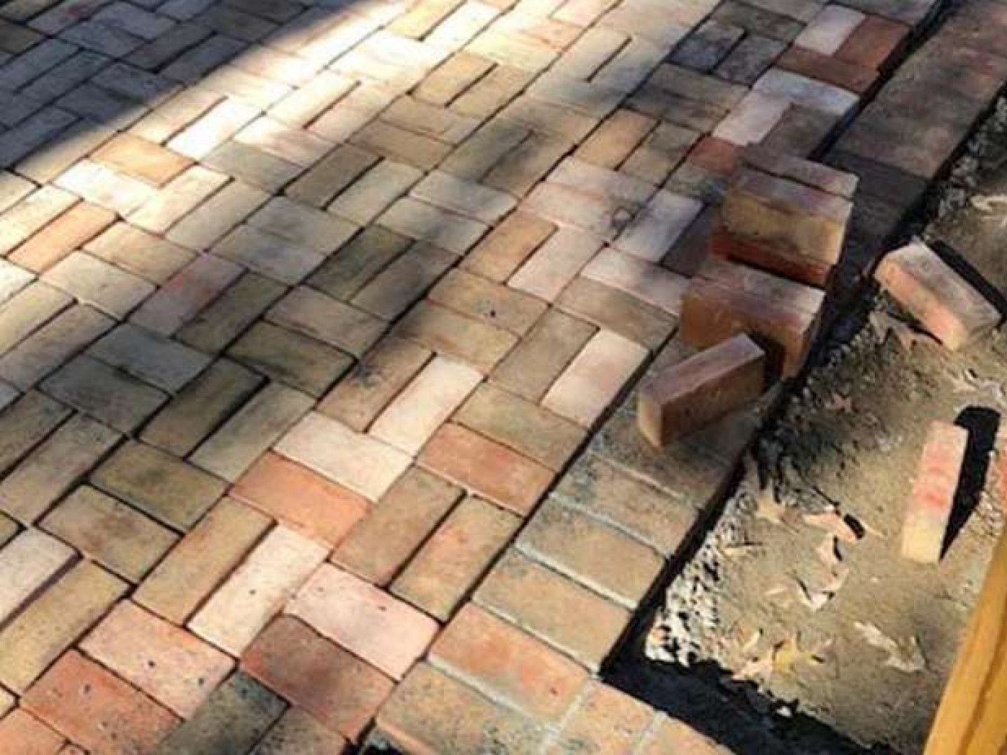 Partially laid brick paver walkway with stacked bricks and exposed sand bed