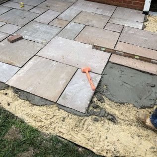 Patio pavers being installed, with an orange mallet, level, and sand base visible