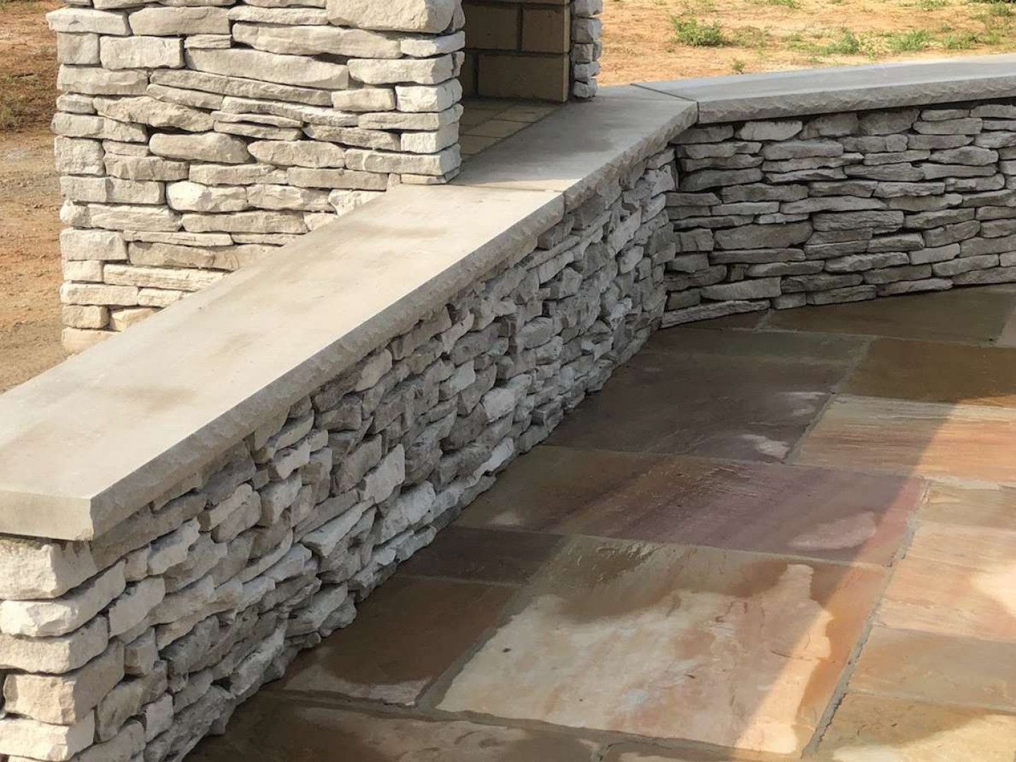 Stone patio with a low stacked-stone wall and beige cap, forming a built-in bench or planter edge.