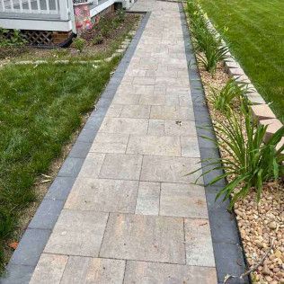 Narrow stone walkway bordered by grass and plants alongside a house