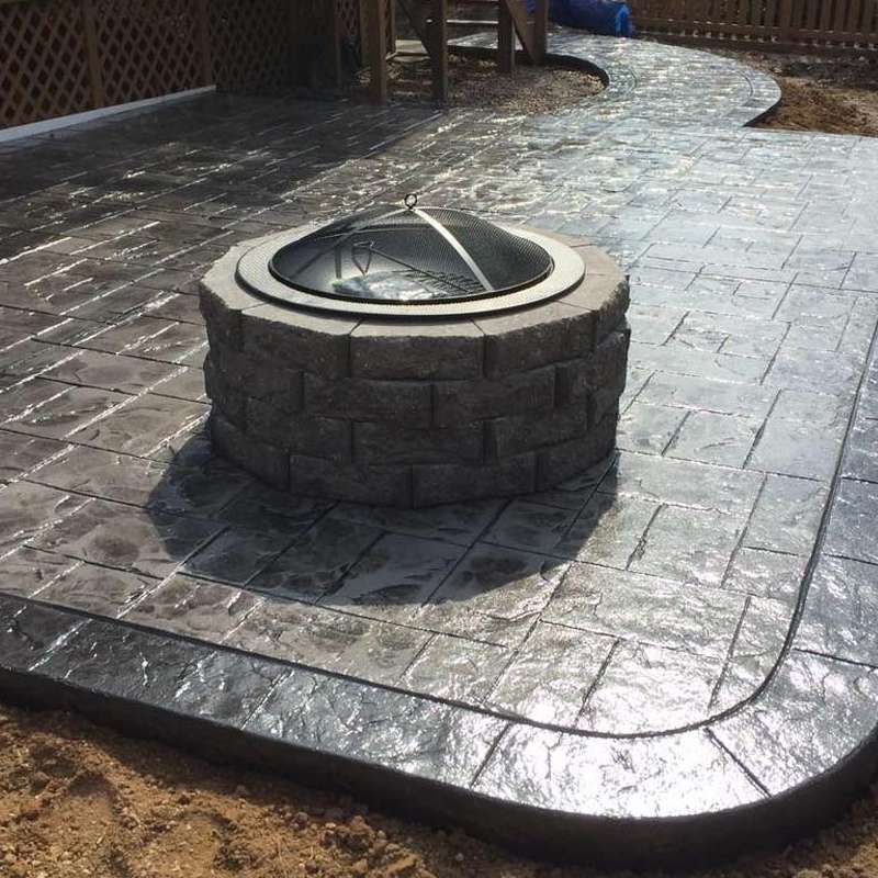 Stone fire pit with a circular glass top on a stamped concrete patio outdoors