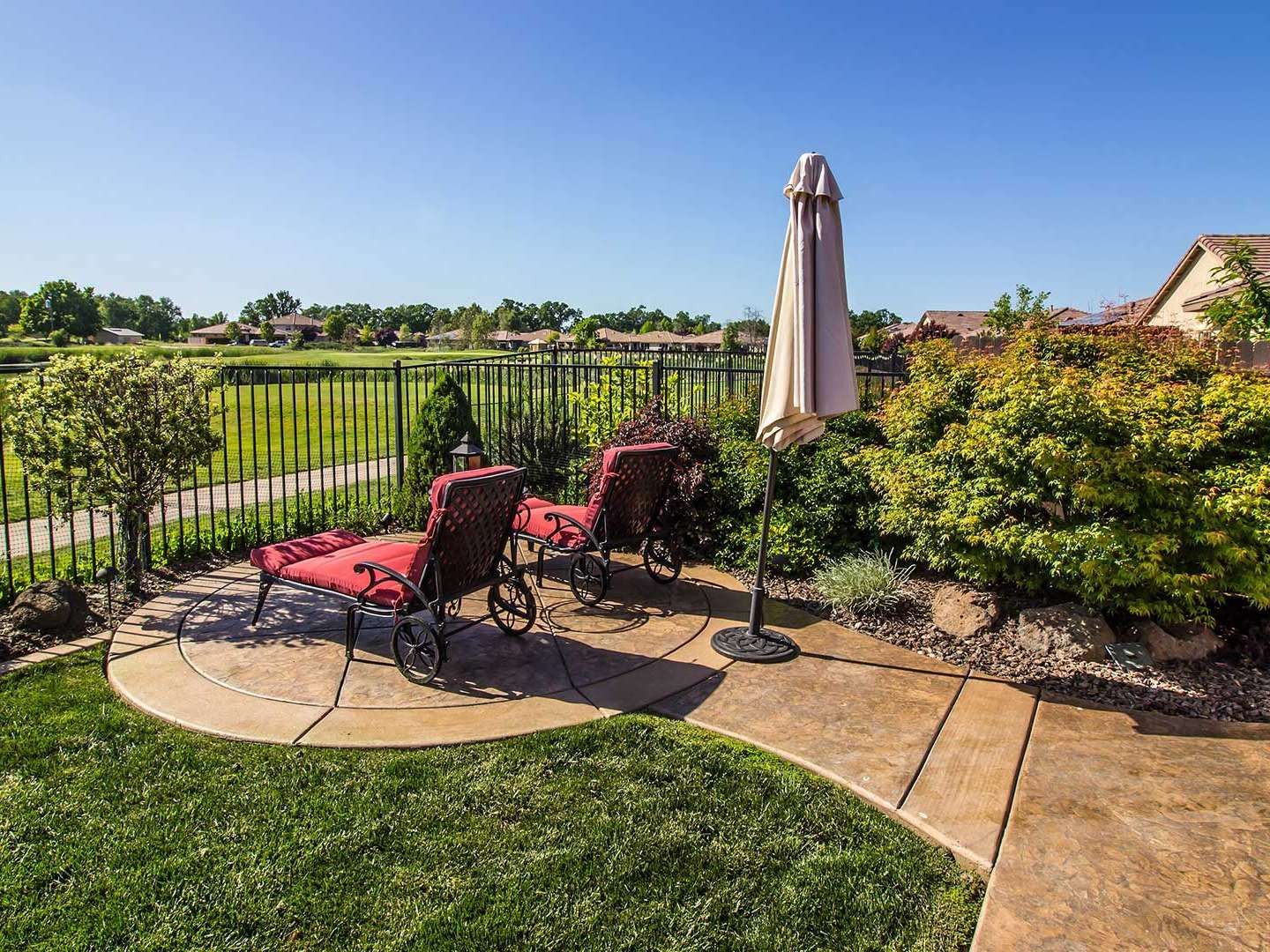 Patio with red lounge chairs, umbrella, and garden view beside a black iron fence