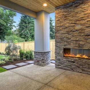 Covered patio with stone fireplace, concrete floor, and landscaped yard beyond.