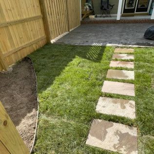 Backyard path with stone pavers set in grass beside a wooden fence and patio area
