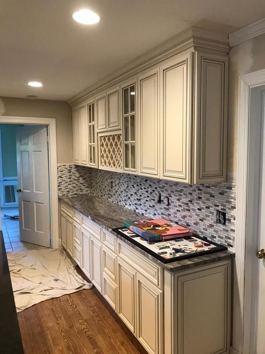 Modern kitchen hallway with cream cabinets, mosaic backsplash, marble floor, and wood flooring.