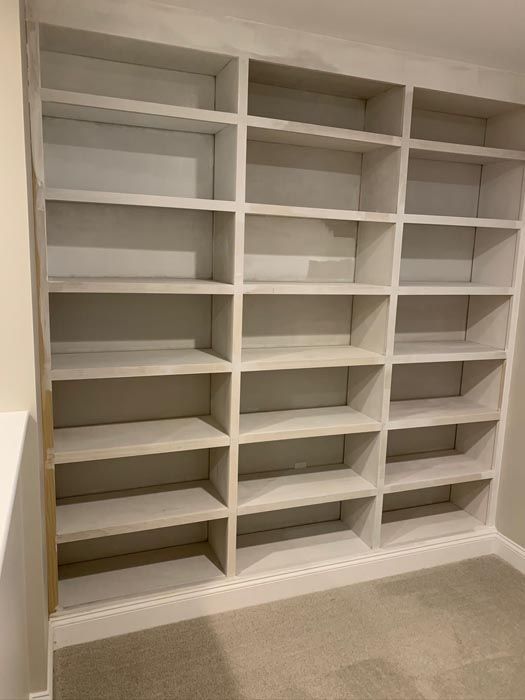 Built-in white shelving unit with multiple empty shelves above beige carpet.