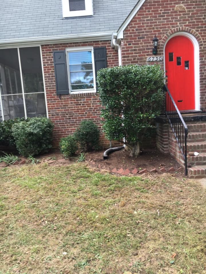Brick house exterior with bright red front door, steps, bushes, and a small lawn.