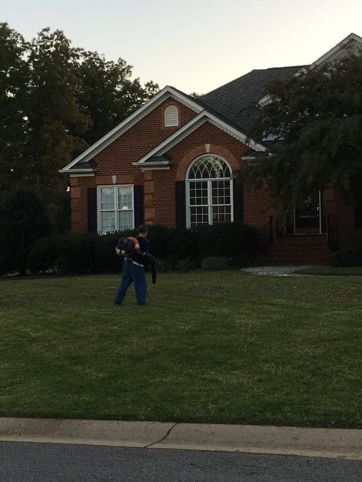 Person mowing a lawn in front of a red brick house with white-trimmed windows.