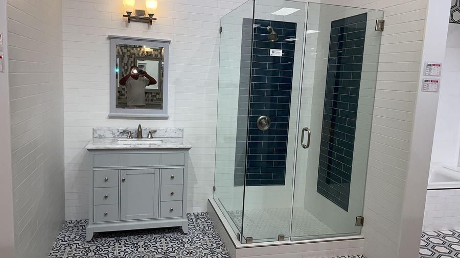 Bathroom showroom with white vanity and mirror, glass shower enclosure, and patterned black-and-white floor tiles