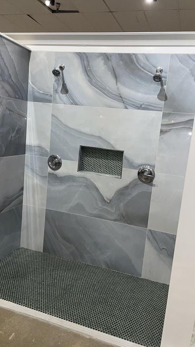 Marble-tiled shower wall with built-in niche, metal fixtures, and pebble-pattern floor.