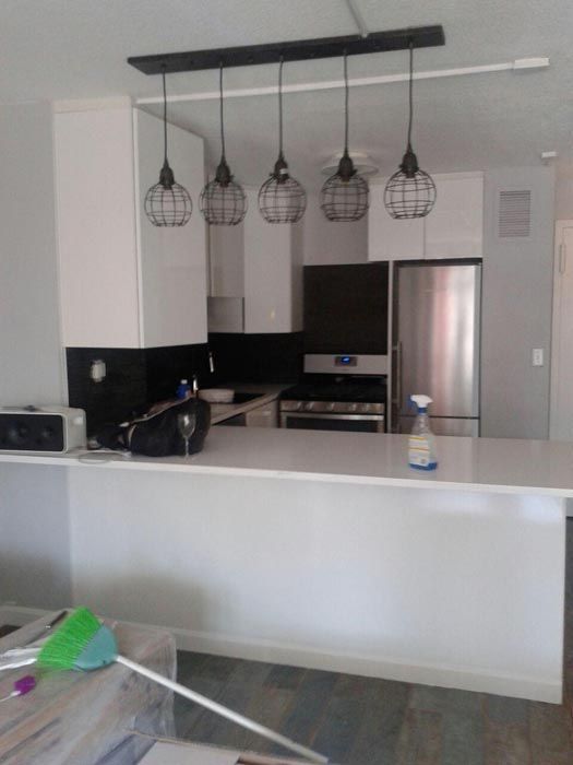 Modern kitchen with white cabinets, black backsplash, island counter, stainless steel fridge, and hanging pendant lights