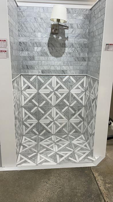 Decorative tiled shower wall with a wall sconce and geometric lower panel in a gray bathroom