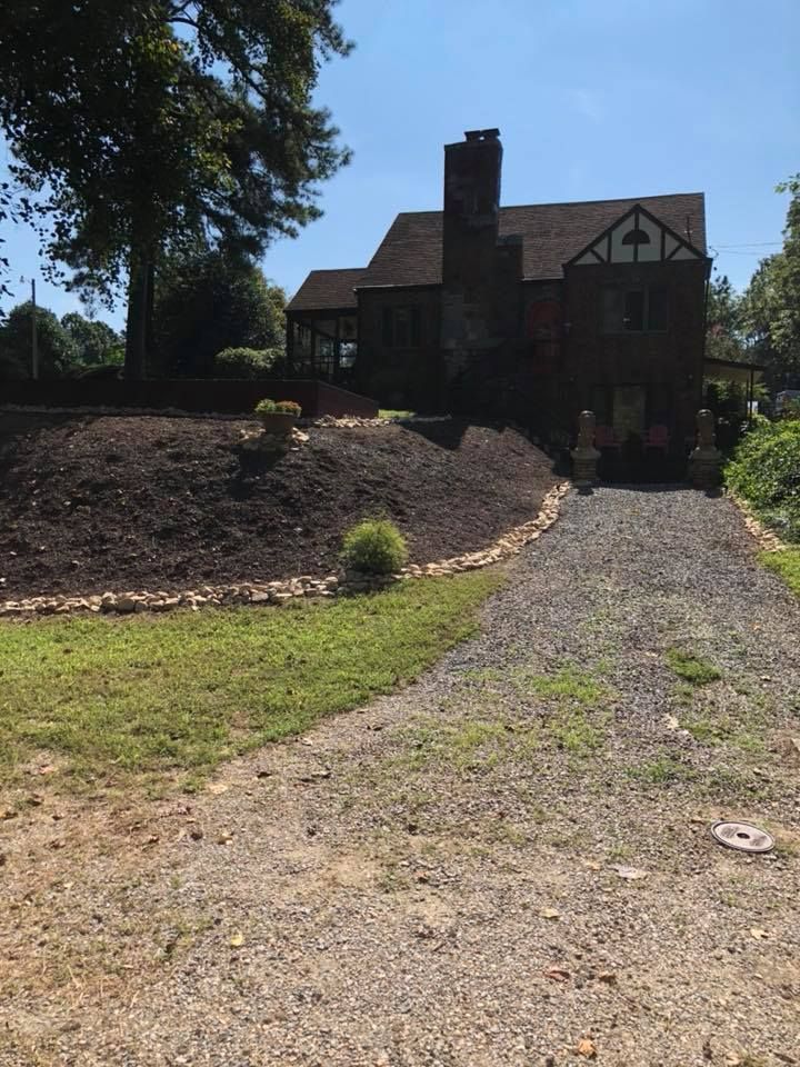 Stone house with gravel driveway, sunlit front yard, and large tree on the left