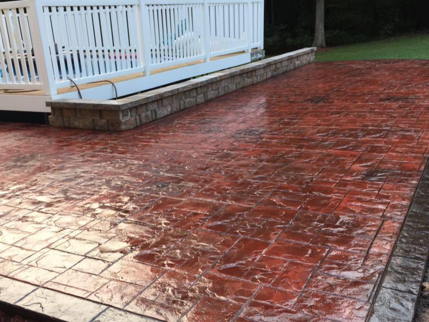 Red stamped concrete patio beside a white-railed deck and house.