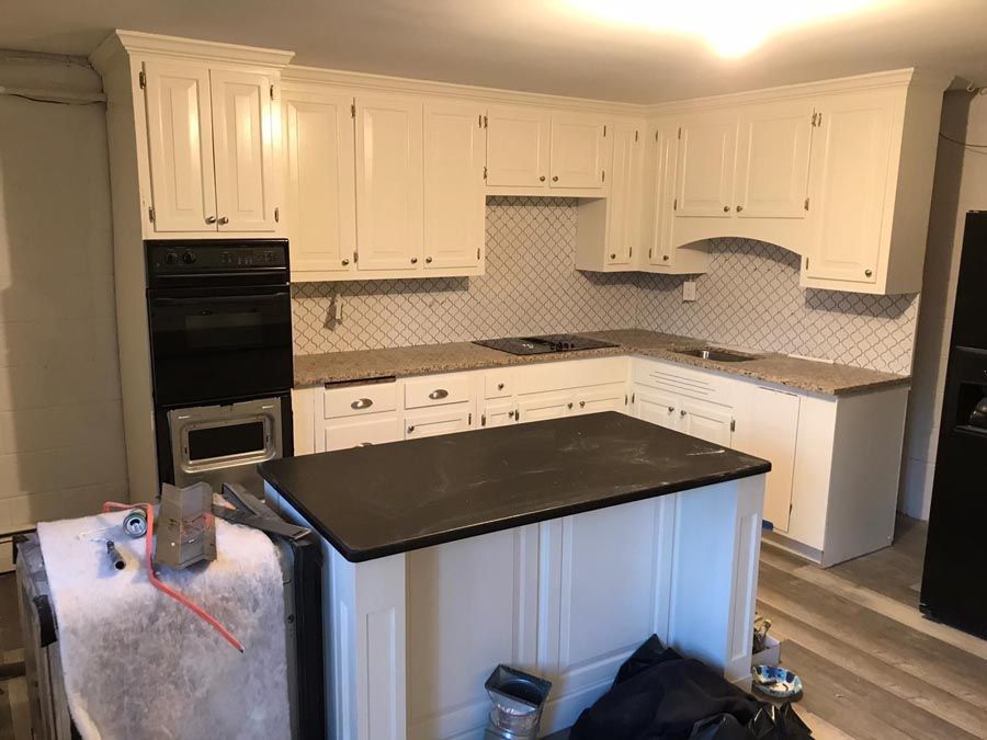 Bright white kitchen with black island countertop, white cabinets, and built-in oven and microwave